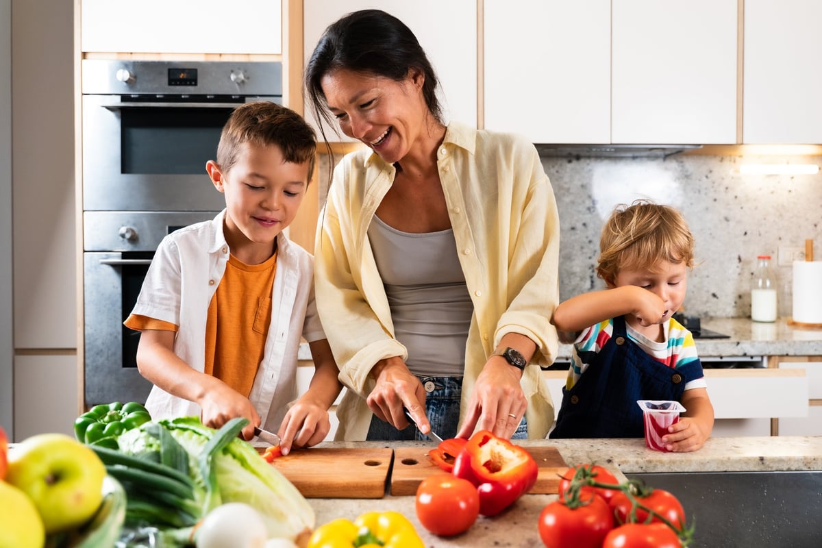 An Asian family preparing fresh vegetables together in a modern kitchen, smiling and learning
